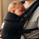Newborn baby snug in 6-in-1 carrier against parent's chest, showing M-position legs for safe hip support