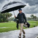 Golfer holding a large double-canopy golf umbrella on a Florida course during a summer rainy season downpour