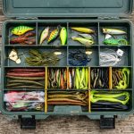 Flat lay of budget tackle boxes and colorful fishing lures on a wooden table.