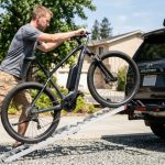 Close-up of hands tightening a heavy e-bike frame clamp on a hitch rack.